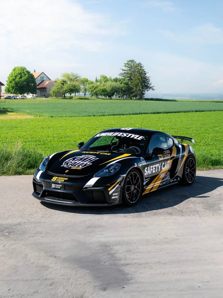 Porsche GT4 en kit déco Safety Car noir et jaune, chemin entre les champs