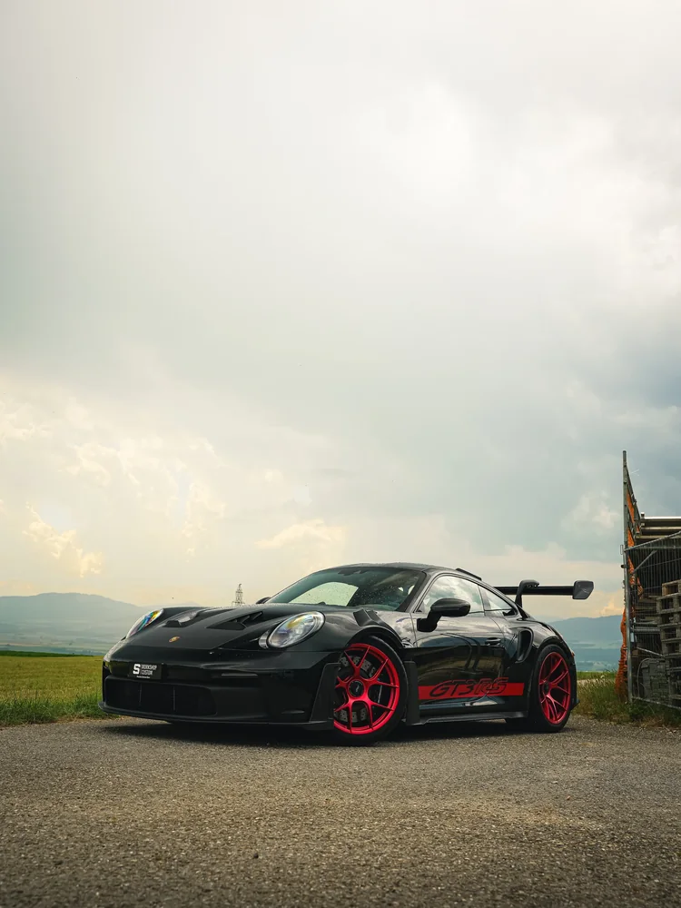 Porsche GT3 RS noire à jantes rouges en full PPF, de trois quarts avant, ciel voilé