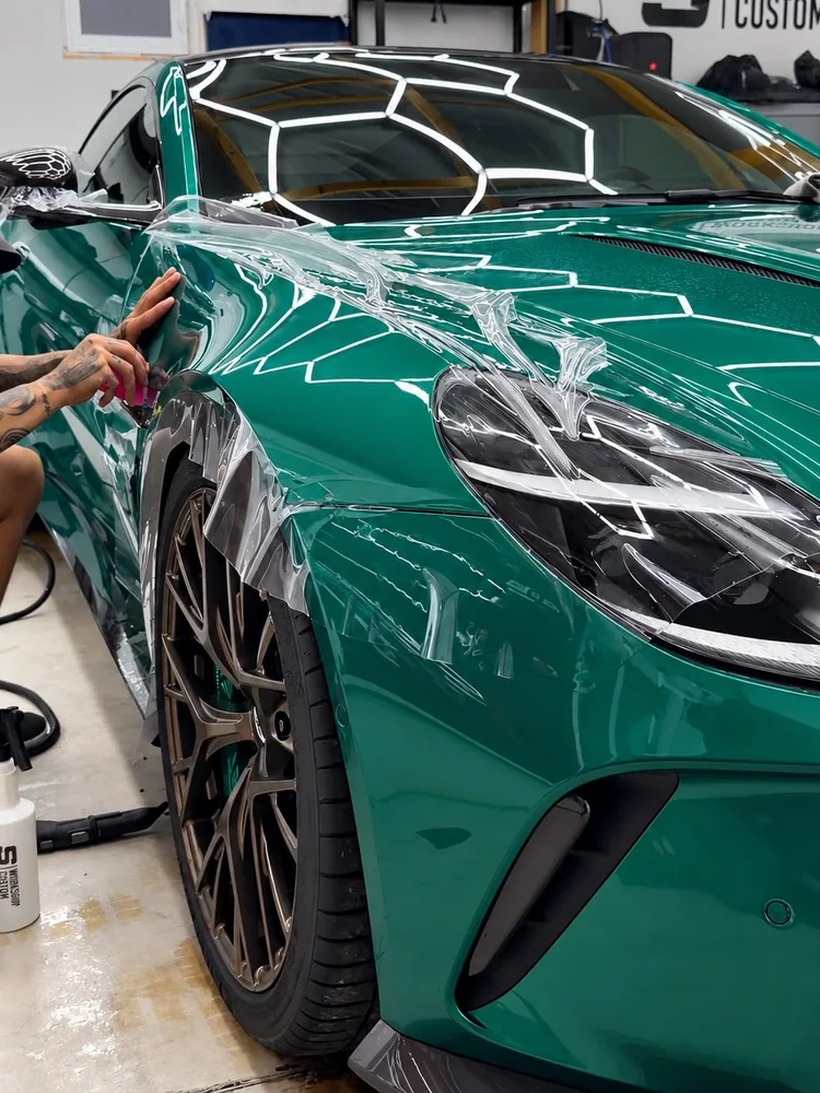 Pose d'un PPF transparent sur l'aile avant d'une voiture verte, à l'atelier